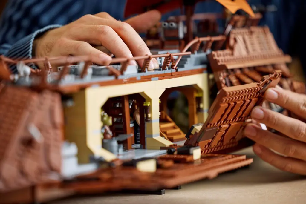 Hands assembling a detailed LEGO ship model.