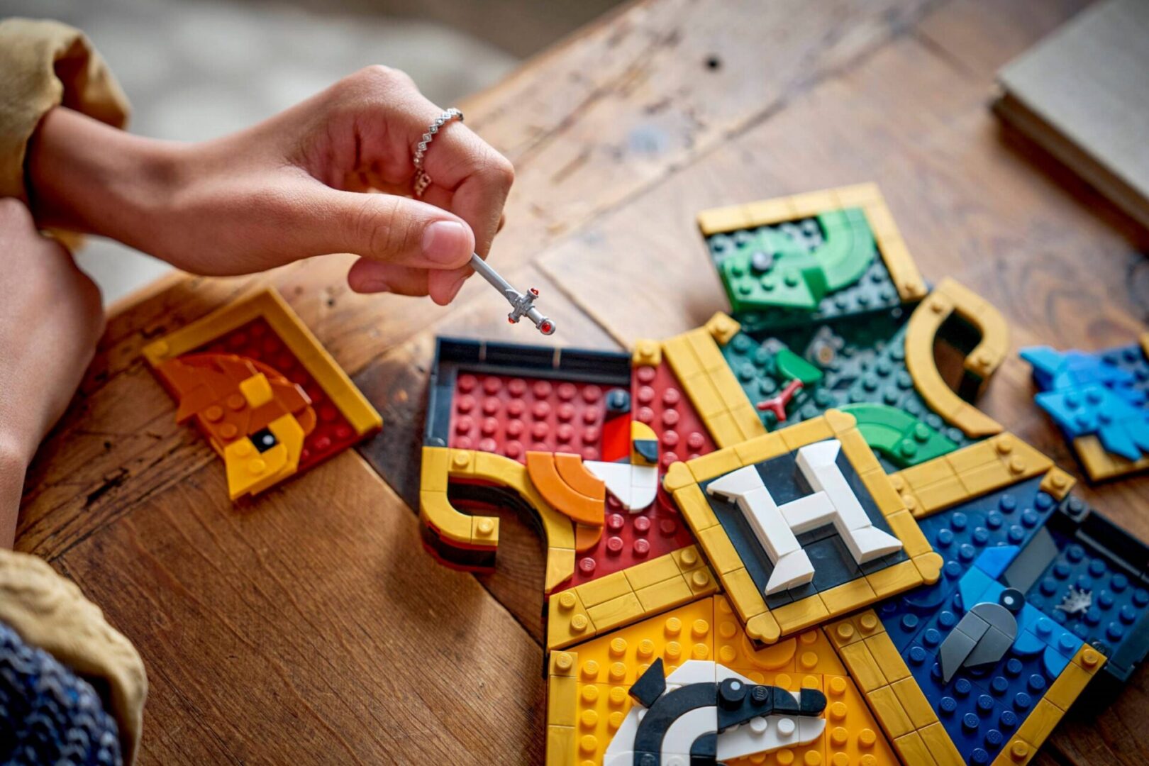 Person assembling colorful LEGO crest on table.